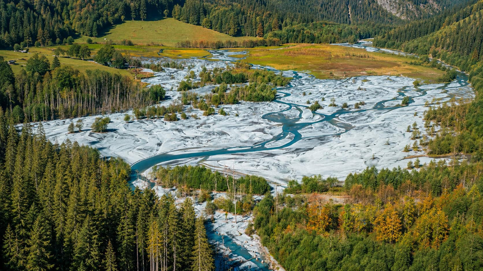 Weitläufige Schwemmebene des Tschingelsees im Kiental bei Griesalp mit türkisfarbenen Wasserläufen und herbstlichem Bergwald